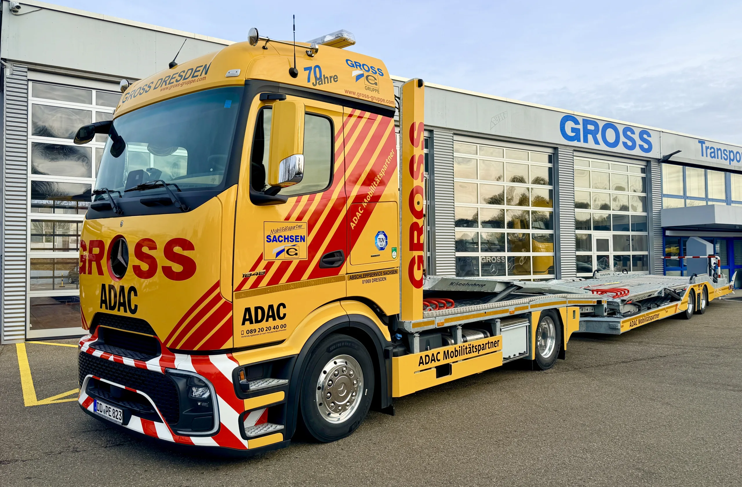 Gelber ADAC-Mobilitäts-Lkw mit auffälligen Streifen vor einem modernen Gebäude der Firma GROSS in Dresden.