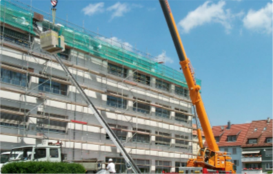 Bauarbeiten an einem mehrstöckigen Gebäude mit Gerüst; Kran hebt Material, Arbeiter in Sicherheitskleidung im Vordergrund.