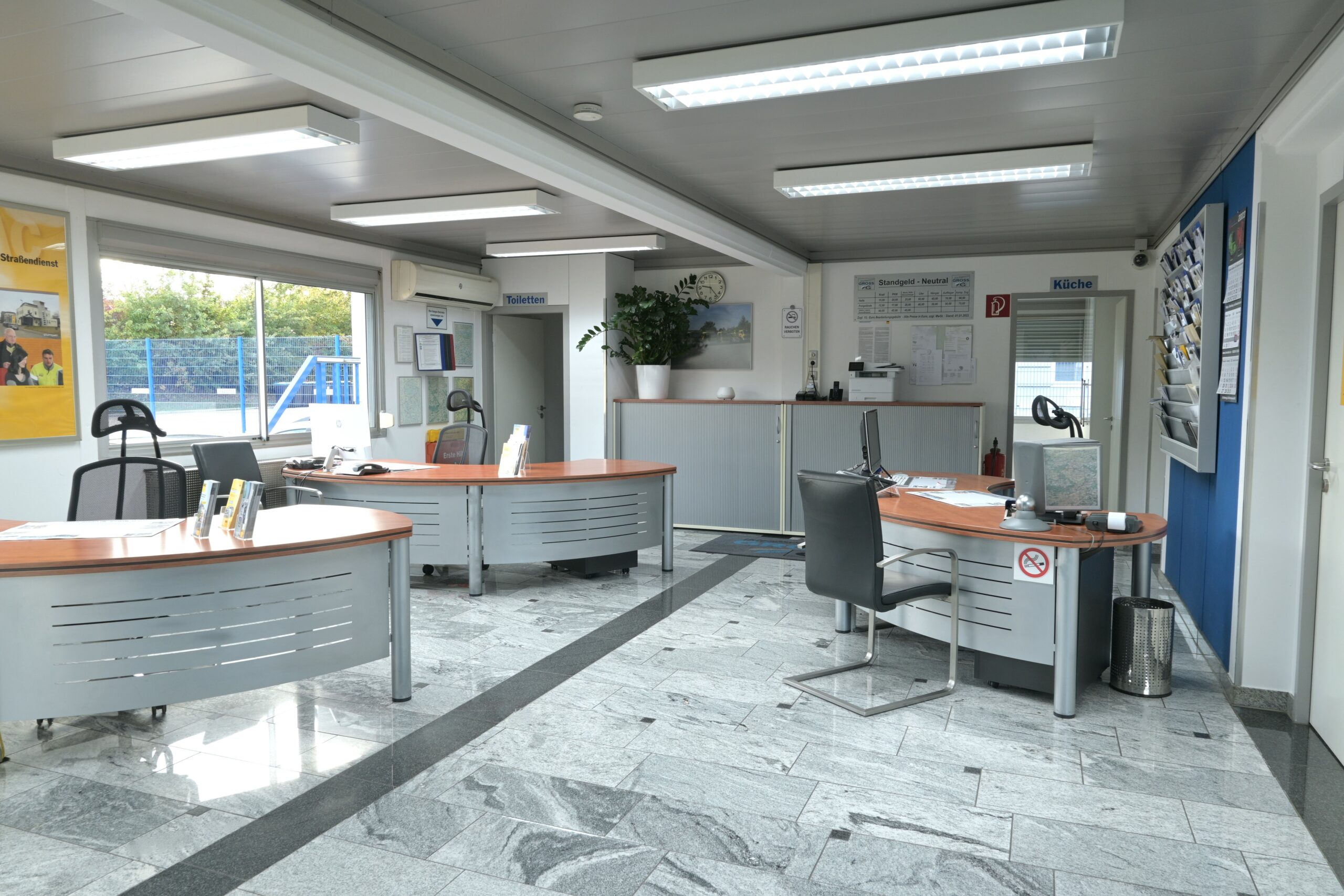 Helles Büro mit vier Schreibtischen, Stühlen, Pflanzen und Informationsmaterial. Fenster mit Ausblick.