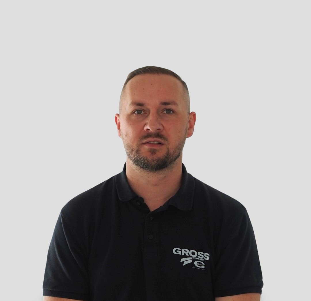 Ein Mann mit kurzem Haar und Bart trägt ein schwarzes Polo-Hemd vor weißem Hintergrund.