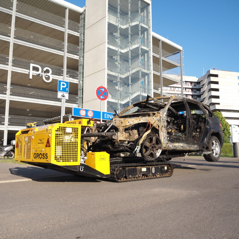 Gelbes Bergungsfahrzeug transportiert ausgeschlachtetes Auto vor Parkhaus P3.