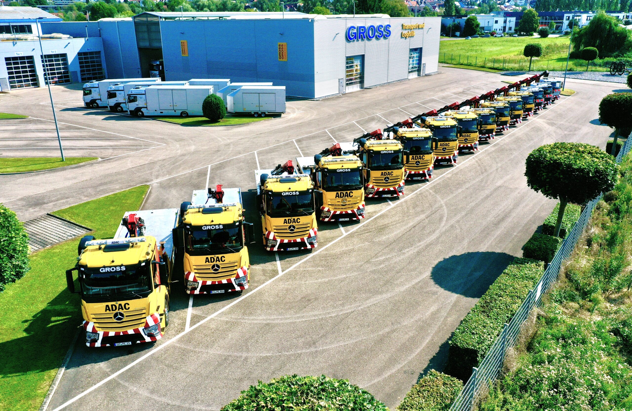 Reihe von gelben ADAC-Abschleppwagen auf Parkplatz vor einem Gebäude mit der Aufschrift GROSS.