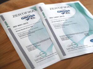 Zwei DEKRA-Zertifikate: ISO 9001:2015 und ISO 14001:2015, ausgestellt für Gross GmbH & Co. KG auf einem Holztisch.
