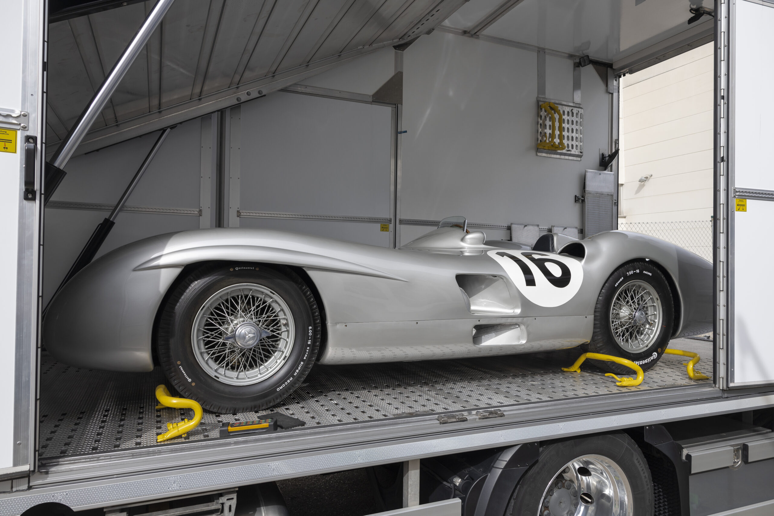 Silberner Rennwagen mit Startnummer 10 steht gesichert auf einem LKW-Anhänger in einer offenen Transportkabine.