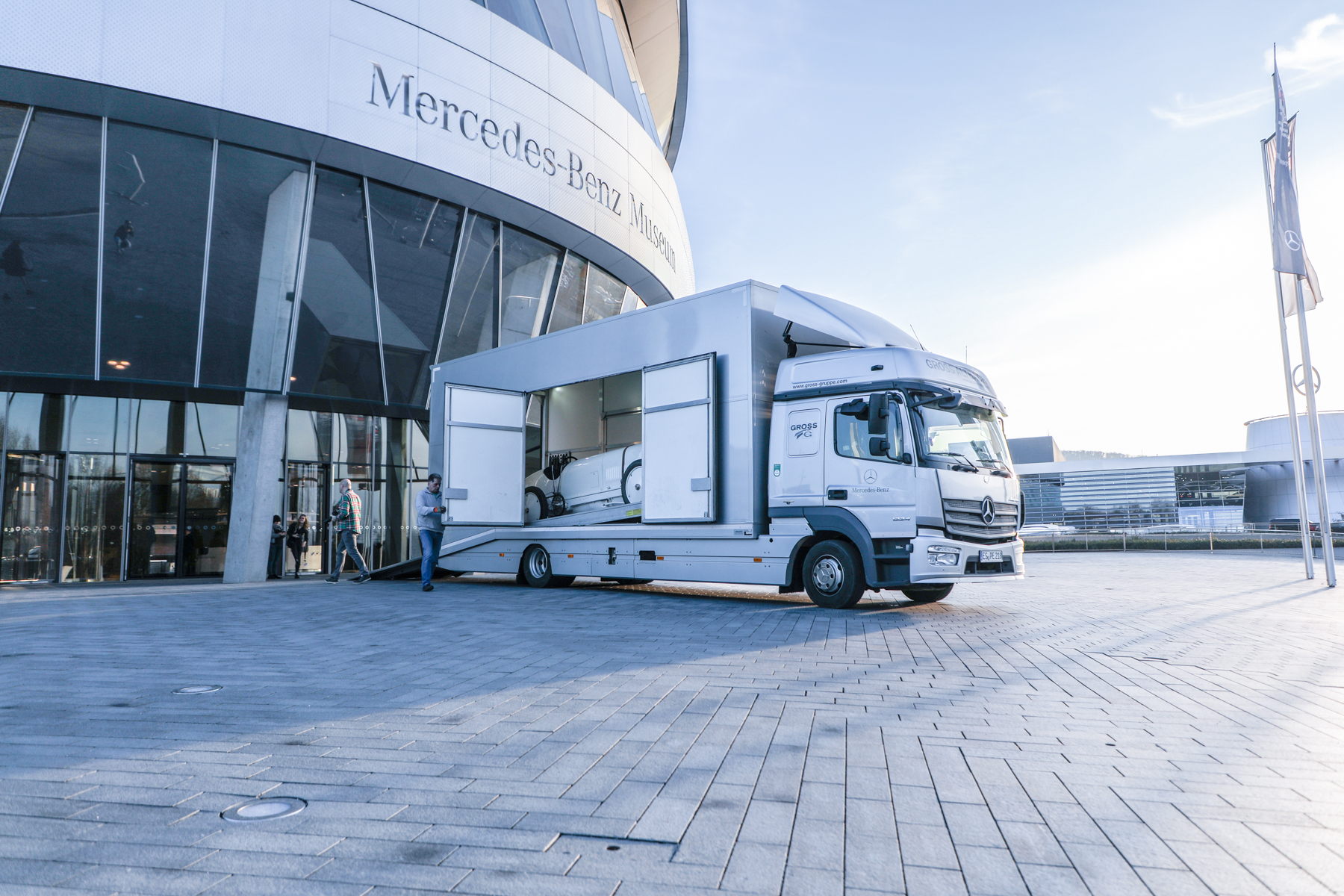 Ein Transporter steht geöffnet vor dem Mercedes-Benz Museum, mit sichtbarem Oldtimer-Auto im Inneren.