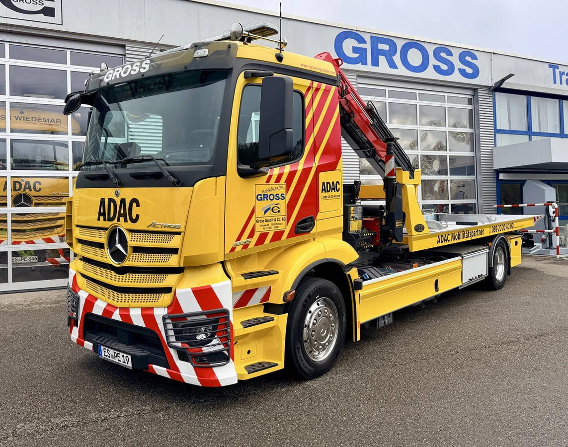 Gelber ADAC Abschleppwagen mit rotem Kran, vor einer Werkstatt mit GROSS-Beschriftung.