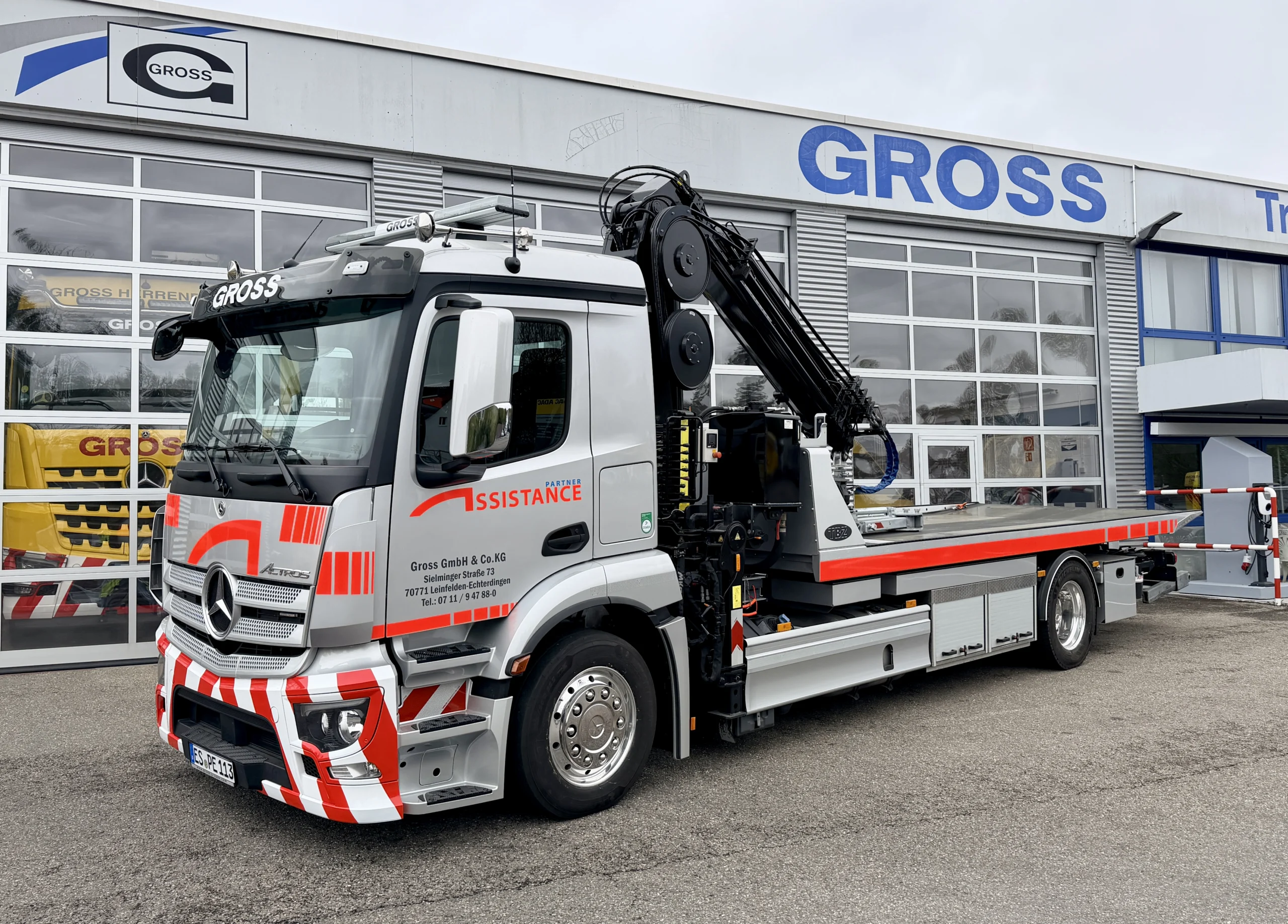 Silberner Lkw mit Kran der Firma Gross vor einem modernen Gewerbegebäude, beschriftet mit „GROSS“.